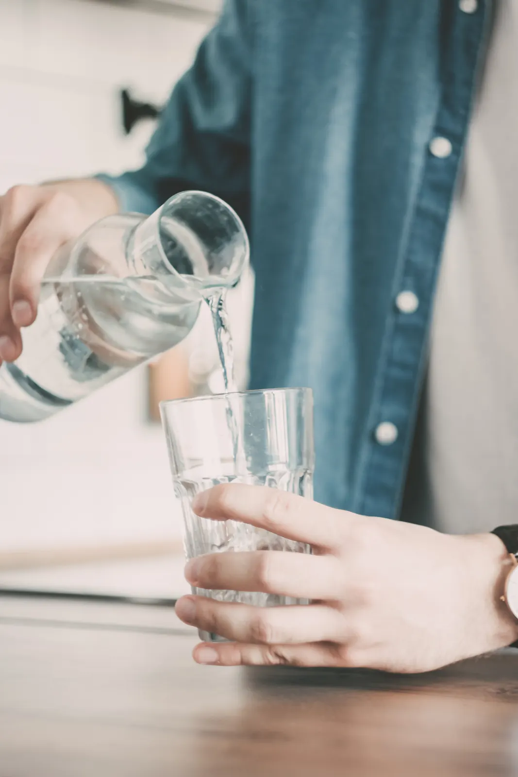 Hand pouring water from a small glass carafe into a tumbler