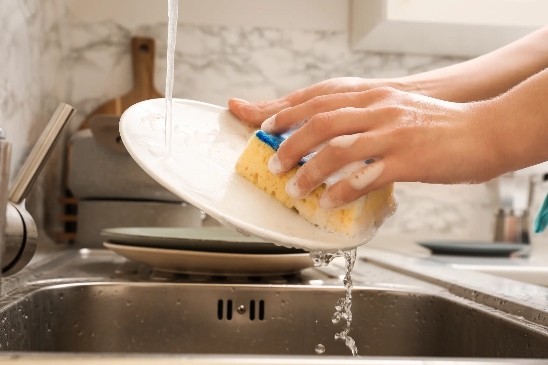 Hands rinsing a plate under running water at a kitchen sink