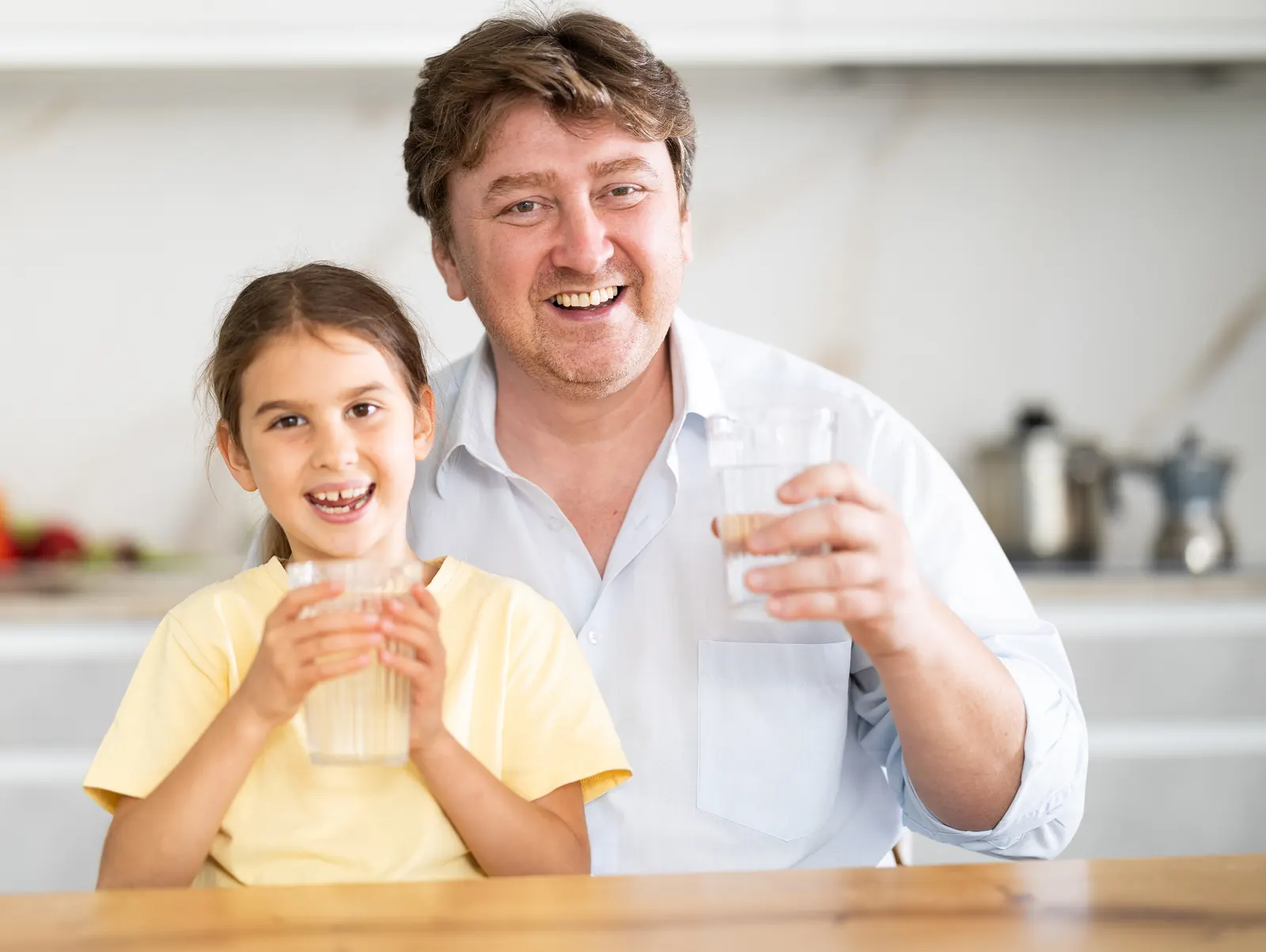Man and girl smiling at a kitchen counter, each holding a glass of water